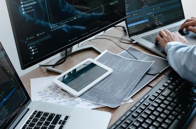 A desk at an office with multiple monitors turned on and papers on the desk